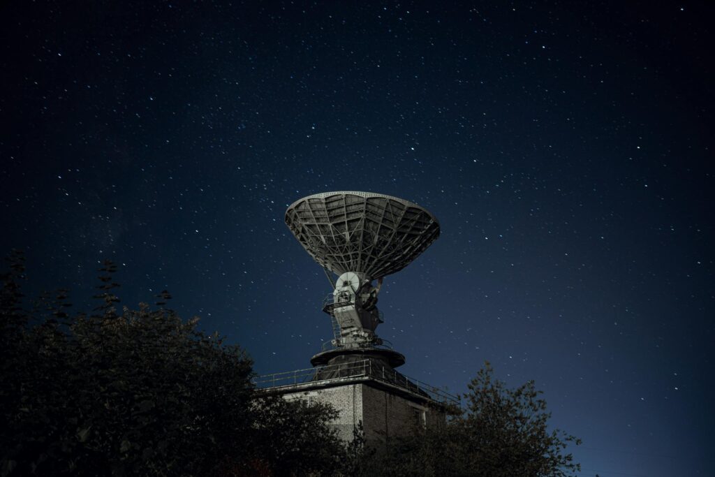 Radio telescope and green lush trees under blue sky with stars at night earth science