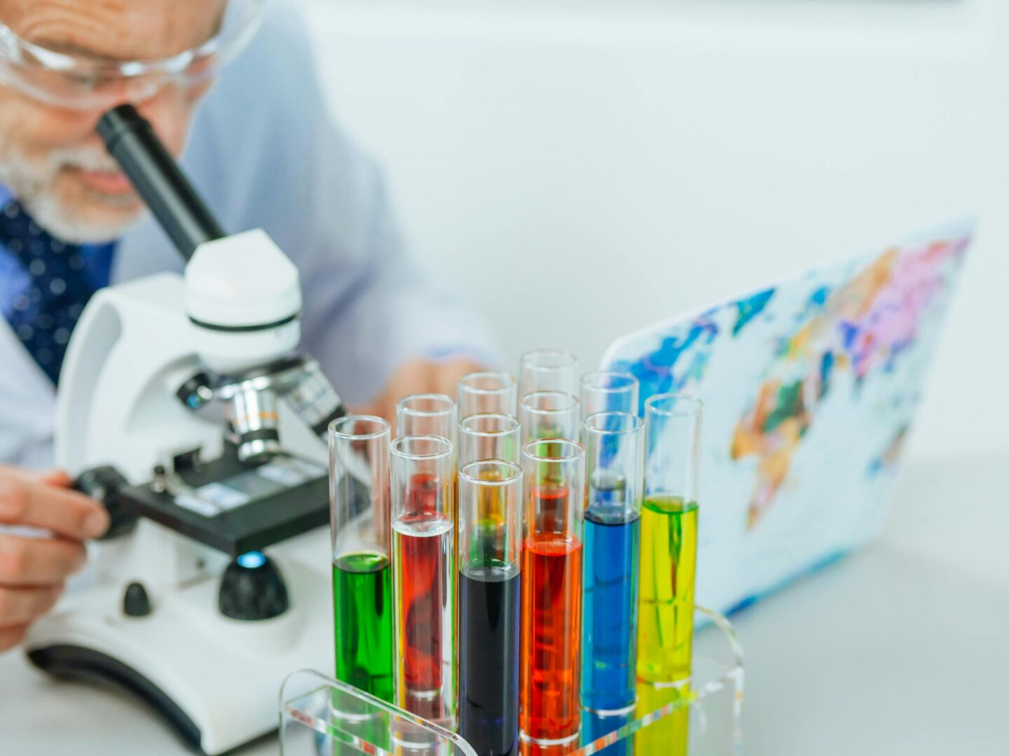 Scientist using microscope with colorful test tubes for research in a laboratory setting.